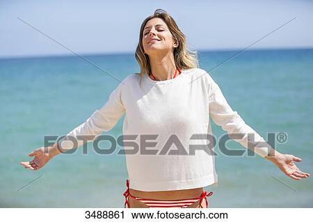 Stock Image - Pretty blonde woman enjoying at the beach with arms opened. Fotosearch
