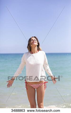 Stock Image - Pretty blonde woman enjoying at the beach with arms opened. Fotosearch
