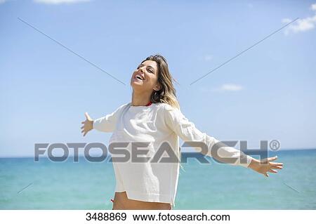 Stock Photo - Pretty blonde woman enjoying at the beach with arms opened. Fotosearch