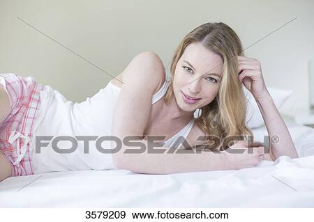 Pretty blonde woman lying in bed smiling at camera View Large Photo Image Stock Photo - Pretty blonde woman lying in bed smiling at camera. Fotosearch