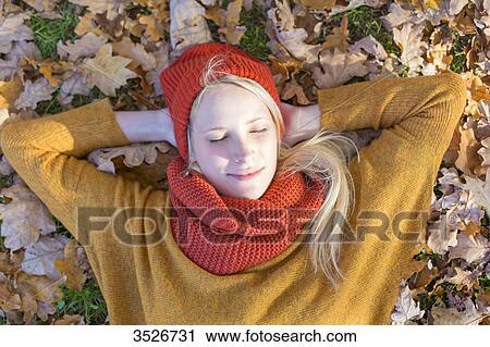 Stock Image - Pretty blonde woman lying in park in autumn with eyes closed. Fotosearch