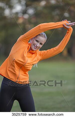 Stock Photo - Pretty blonde woman stretching in park and smiling at camera. Fotosearch