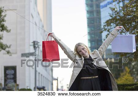 Pretty blonde woman with arms raised and shopping bags walking in downtown View Large Photo Image Stock Image - Pretty blonde woman with arms raised and shopping bags walking in downtown. Fotosearch