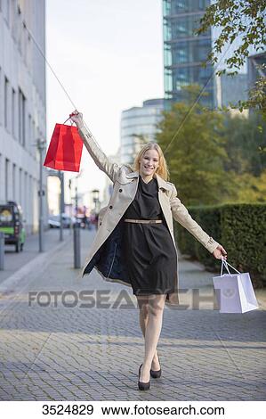 Stock Photo - Pretty blonde woman with arms raised and shopping bags walking in downtown. Fotosearch