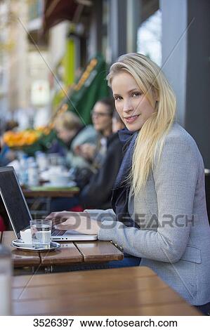 Stock Photo - Pretty blonde woman with laptop in a Cafe smiling at camera. Fotosearch