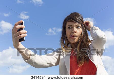 Pretty brunette woman doing a selfie with smartphone View Large Photo Image Picture - Pretty brunette woman doing a selfie with smartphone. Fotosearch