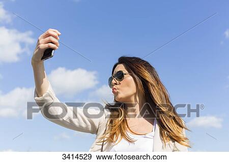 Pretty brunette woman doing a selfie with smartphone View Large Photo Image Stock Photo - Pretty brunette woman doing a selfie with smartphone. Fotosearch