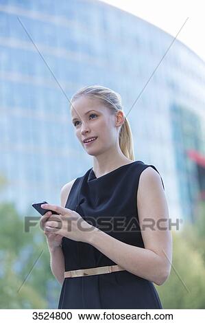 Pretty elegant woman checking her mobile in front of a office building in downtown View Large Photo Image Stock Image - Pretty elegant woman checking her mobile in front of a office building in downtown. Fotosearch