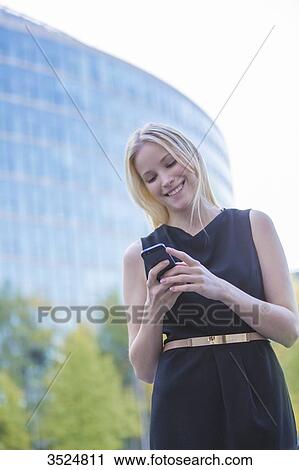Stock Image - Pretty elegant woman checking her mobile in front of a office building in downtown. Fotosearch