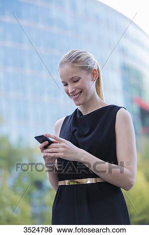 Pretty elegant woman checking her mobile in front of a office building in downtown View Large Photo Image Stock Photo - Pretty elegant woman checking her mobile in front of a office building in downtown. Fotosearch