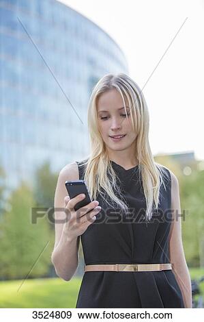 Stock Photo - Pretty elegant woman checking her mobile in front of a office building in downtown. Fotosearch