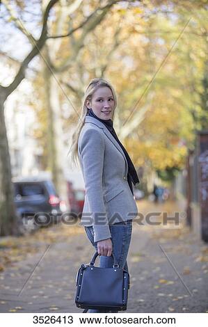 Stock Image - Pretty elegant woman walking with handbag in citycenter. Fotosearch