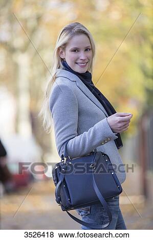 Stock Photo - Pretty elegant woman walking with handbag in citycenter and smiling at camera. Fotosearch