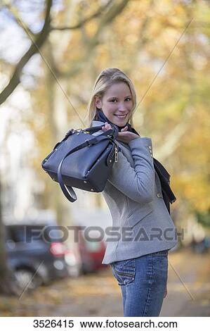 Stock Photography - Pretty elegant woman walking with handbag in citycenter and smiling at camera. Fotosearch