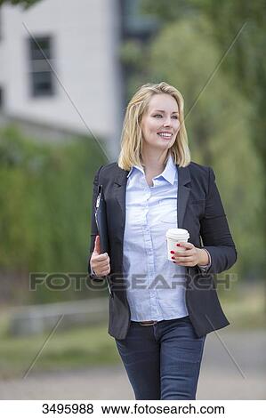 Stock Photo - Pretty executive woman walking with coffee outdoors. Fotosearch