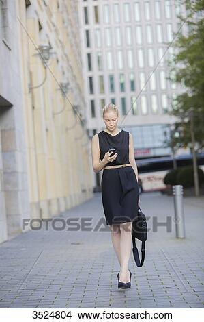 Picture - Pretty executive woman with bag checking her mobile in Downtown. Fotosearch