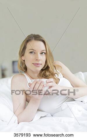 Stock Image - Pretty pensive woman enjoying a tea in bed. Fotosearch