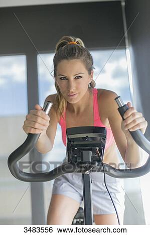 Stock Photograph - Pretty woman doing spinning bike in fitness center. Fotosearch