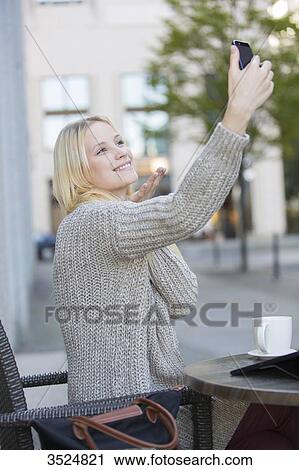 Stock Image - Pretty young woman doing a selfie in a Cafe in city center sending a kiss. Fotosearch