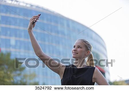 Pretty young woman taking a selfie in front of an Office Building View Large Photo Image Stock Image - Pretty young woman taking a selfie in front of an Office Building. Fotosearch