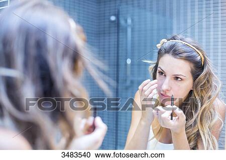 Stock Image - Reflection of a young woman in a mirror applying make-up. Fotosearch
