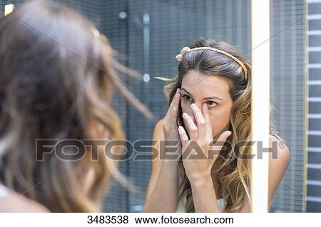 Reflection of a young woman in a mirror applying make-up View Large Photo Image Stock Photo - Reflection of a young woman in a mirror applying make-up. Fotosearch
