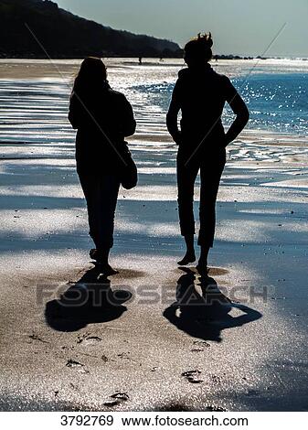 Stock Photo - Silhoutte of two women walking on the beach. Fotosearch