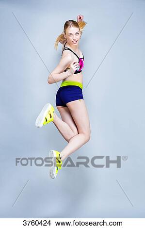Smiling young woman dressed for fitness, back, jumps on a gray background View Large Photo Image Picture - Smiling young woman dressed for fitness, back, jumps on a gray background. Fotosearch