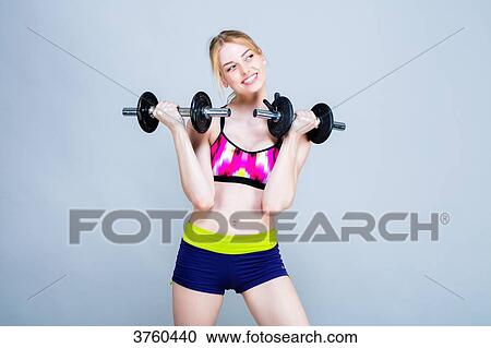 Smiling young woman dressed in fitness, front, holds dumbbells View Large Photo Image Stock Image - Smiling young woman dressed in fitness, front, holds dumbbells. Fotosearch