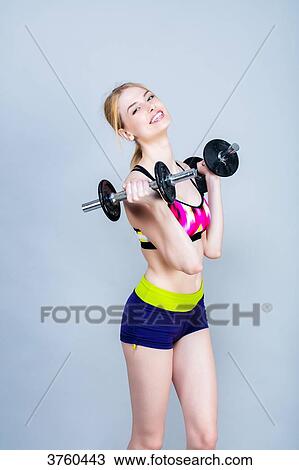 Stock Image - Smiling young woman dressed in fitness, front, holds dumbbells. Fotosearch