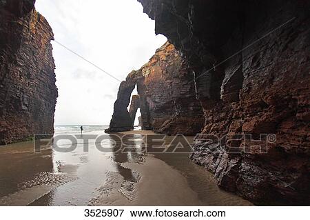 Spain, Galicia. Ribadeo. Tiny shape between very large rocks. Las Catedrales beach. View Large Photo Image Stock Photo - Spain, Galicia. Ribadeo. Tiny shape between very large rocks. Las Catedrales beach.. Fotosearch