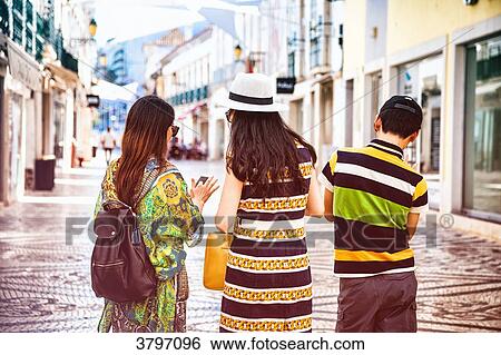 Stock Photograph - Three tourists back, looking a mobile phone in a street in the city of Faro, Algarve region, Portugal. Fotosearch