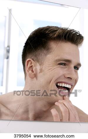 topless man, looking in the mirror, looking at his teeth in the mirror, finger on his chin, smiling, window in the background View Large Photo Image Picture - topless man, looking in the mirror, looking at his teeth in the mirror, finger on his chin, smiling, window in the background. Fotosearch