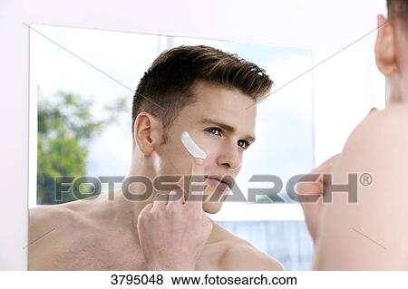 topless man, looking in the mirror, putting some moisturising cream on his face with his finger, window in the background, back of the shoulder blur on the foreground View Large Photo Image Stock Photo - topless man, looking in the mirror, putting some moisturising cream on his face with his finger, window in the background, back of the shoulder blur on the foreground. Fotosearch