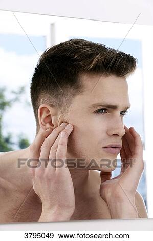 Stock Photo - topless man, looking in the mirror, looking at his face in the mirror, looking at his eye wrinkles, window in the background. Fotosearch