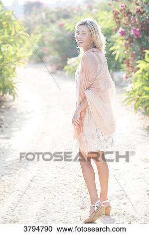 Stock Image - View of a smiling woman in a way a flower garden.. Fotosearch