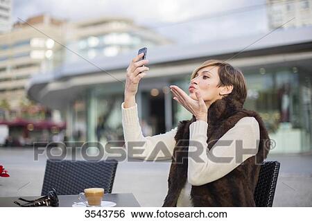 Woman doing a selfie outdoors in a Cafe, sending a kiss View Large Photo Image Stock Photograph - Woman doing a selfie outdoors in a Cafe, sending a kiss. Fotosearch
