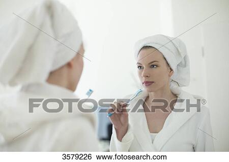 Woman in bathrobe brushing her teeth in front of the mirror View Large Photo Image Stock Photograph - Woman in bathrobe brushing her teeth in front of the mirror. Fotosearch