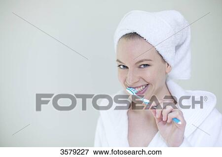 Woman in bathrobe brushing her teeth and smiling at camera View Large Photo Image Stock Photo - Woman in bathrobe brushing her teeth and smiling at camera. Fotosearch