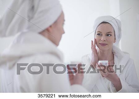 Woman in bathrobe using moisturizer in front of the mirror View Large Photo Image Stock Image - Woman in bathrobe using moisturizer in front of the mirror. Fotosearch