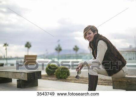 Woman sitting on a bench in citycenter close to the harbour smiling at camera View Large Photo Image Stock Photo - Woman sitting on a bench in citycenter close to the harbour smiling at camera. Fotosearch