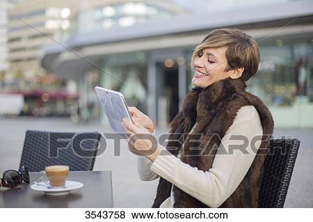 Woman smiling with tablet in a Cafe outdoors View Large Photo Image Stock Photo - Woman smiling with tablet in a Cafe outdoors. Fotosearch
