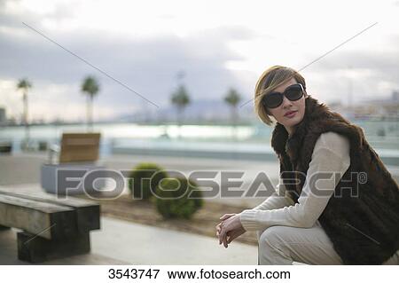 Woman with sunglasses sitting on a bench in citycenter close to the harbour View Large Photo Image Stock Photo - Woman with sunglasses sitting on a bench in citycenter close to the harbour. Fotosearch