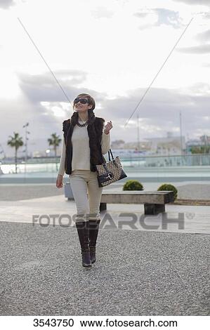 Stock Image - Woman with sunglasses walking with handbag in citycenter close to the harbour. Fotosearch