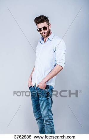 Stock Photo - Young man standing in shirt, side, hands in pockets, looking toward the lens. Fotosearch