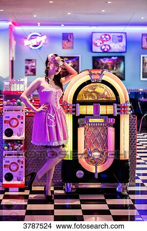 Picture - Young Pin Up, listening to music from a jukebox, looking toward the lens. Fotosearch