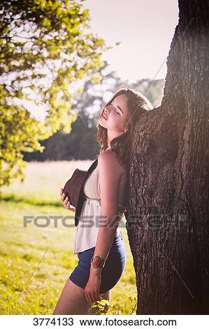 Young woman back to a tree poses against day View Large Photo Image Stock Image - Young woman back to a tree poses against day. Fotosearch