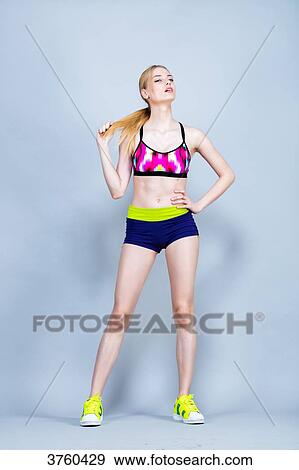 Stock Photo - Young woman, dressed in fitness, front, holding her hair under a gray background. Fotosearch