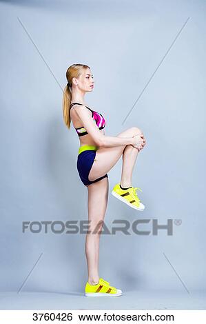 Young woman, dressed in fitness, profile, holding his knee under a gray background View Large Photo Image Stock Photograph - Young woman, dressed in fitness, profile, holding his knee under a gray background. Fotosearch