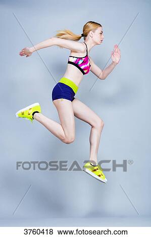 Stock Photo - Young woman holding fitness, profile, courses and jumps on a gray background. Fotosearch